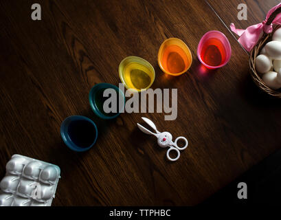 High angle view of dye in colorful bowls with eggs and spoon wooden table during easter Stock Photo