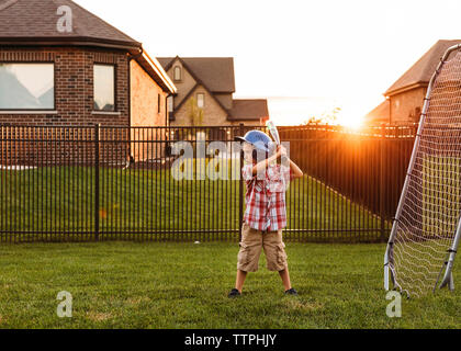 Boy playing baseball in backyard during sunset Stock Photo