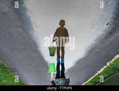 Upside down image of boy standing on wet road while carrying bucket Stock Photo