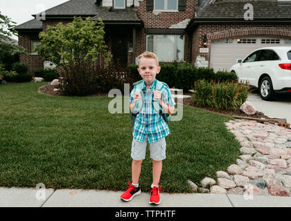 Portrait of boy with backpack standing on footpath against house Stock Photo