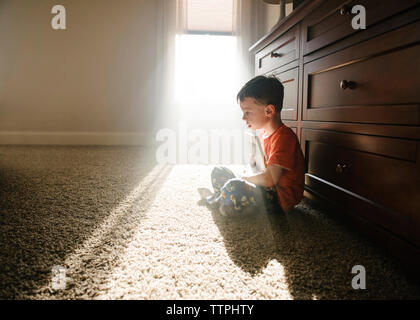 Side view of thoughtful boy with book sitting on rug at home Stock Photo