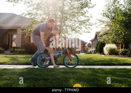 Father assisting son in riding bicycle on road against sky Stock Photo
