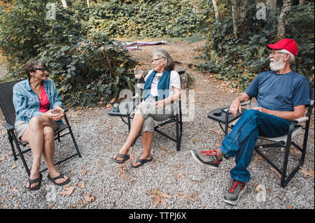 High angle view of friends talking while sitting on chairs in forest Stock Photo