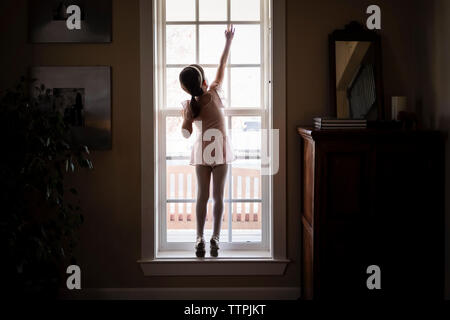 Rear view of girl in ballet costume closing window at home Stock Photo