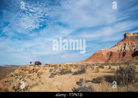 Distant view of woman standing by car on top of mountain against sky Stock Photo