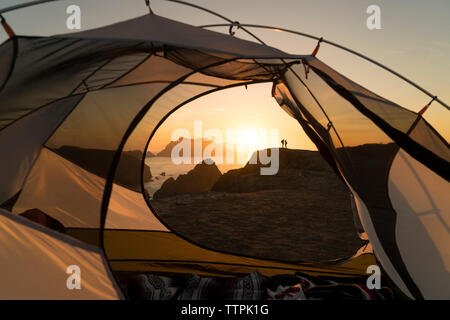 Distant view of couple standing on rock formation seen through tent Stock Photo