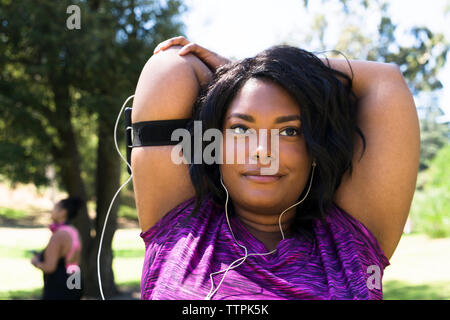 Confident woman looking away while stretching arms at park with female friend in background Stock Photo