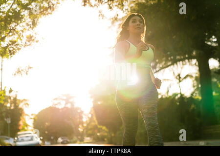 Low angle view of woman jogging in park during sunny day Stock Photo