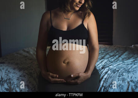 Midsection of pregnant woman touching stomach while sitting on bed at home Stock Photo