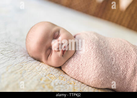 Close-up of baby girl sleeping while wrapped in blanket on bed Stock Photo