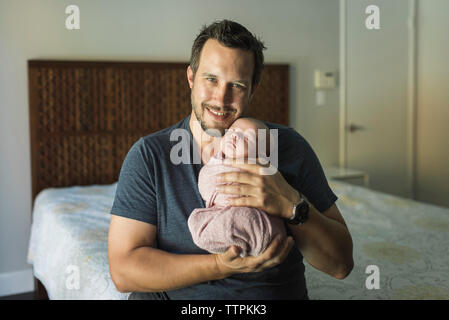 Portrait of happy father carrying newborn daughter in bedroom Stock Photo