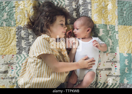 Overhead view of girl lying with baby boy on bed at home Stock Photo