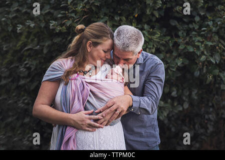 Happy couple with newborn daughter standing against plants at backyard Stock Photo