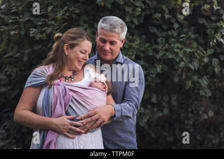 Couple with newborn daughter standing against plants at backyard Stock Photo