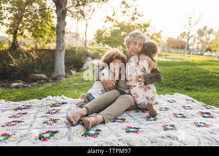 Portrait of grandmother embracing grandchildren on picnic blanket at park Stock Photo