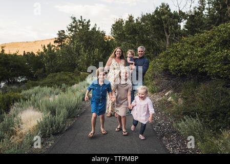 Happy parents looking at daughters holding hands while walking on road against trees in forest Stock Photo