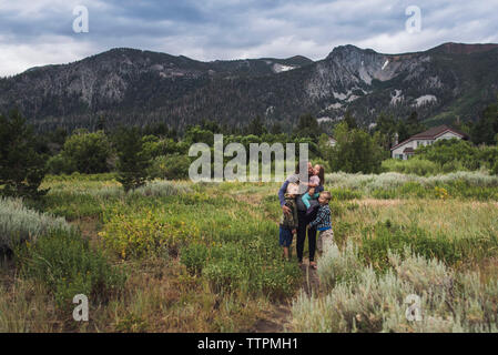 Happy mother with children standing on grassy landscape against cloudy sky in forest Stock Photo