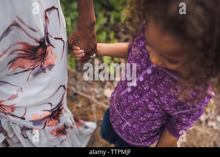 Midsection of mother holding daughter's hand while standing on field in park Stock Photo