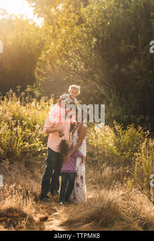 Romantic parents with daughters standing on field against trees in park Stock Photo