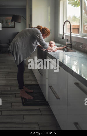 Side view of mother bathing cute son in kitchen sink at home Stock Photo