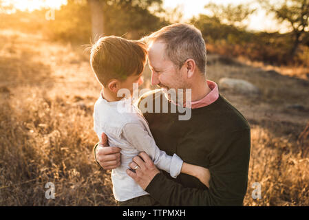 Young boy and father facing each other embracing in California field Stock Photo