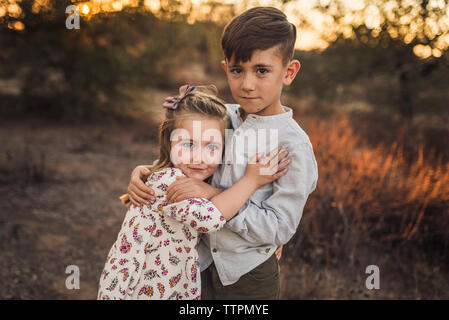 Young girl and boy hugging each other in California field at sunset Stock Photo