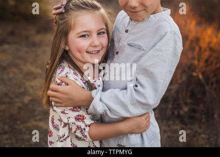 Young girl embraced by brother in California field at sunset Stock Photo