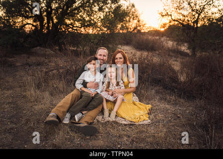 ortrait of family sitting on blanket in California field at sunset Stock Photo