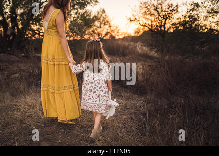 Young girl holding mothers hand while walking away in California field