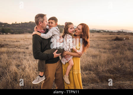 Young boy and girl held by parents in California field during sunset Stock Photo