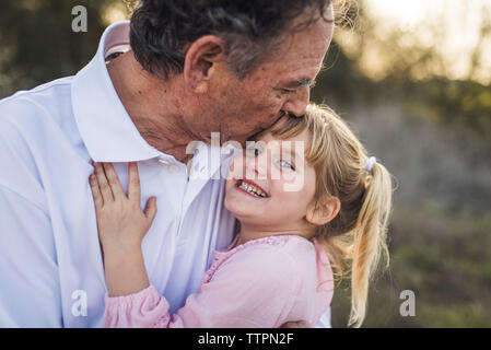 Grandfather hugging young granddaughter and kissing her forehead Stock Photo