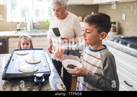 Young boy cooking pancakes with grandma and sister in kitchen Stock Photo