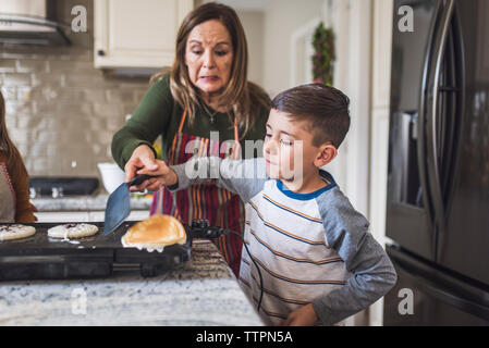 Grandson and grandmother flip pancakes, making breakfast in kitchen Stock Photo