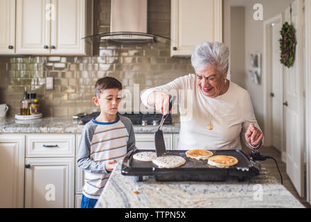 Great grandma and great grandson making pancakes in kitchen Stock Photo