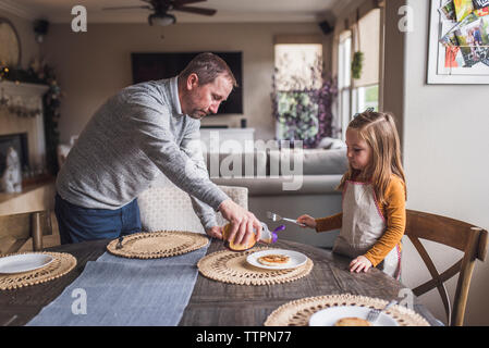 Father helping daughter put syrup on her pancakes for breakfast Stock Photo