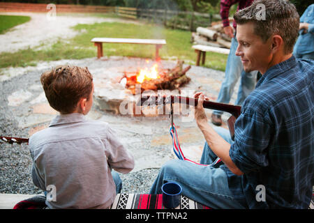 Smiling brothers playing guitar at campsite in forest Stock Photo