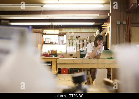 Carpenter using laptop computer while standing at table in workshop Stock Photo