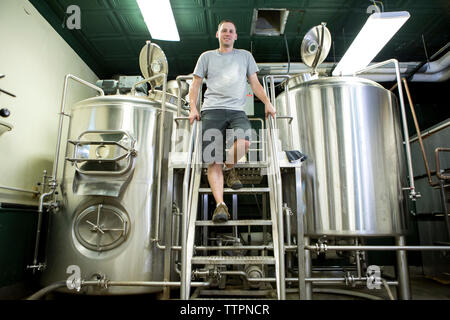 Low angle portrait of confident businessman standing against storage tanks at winery Stock Photo