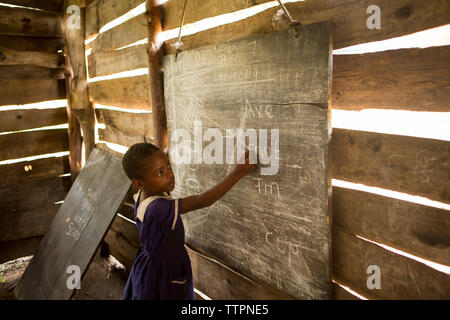Side view of girl writing on blackboard in classroom Stock Photo