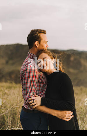 Side view of young couple embracing while standing on field Stock Photo