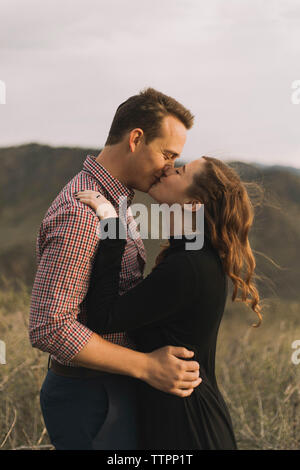 Side view of loving young couple kissing on mouth against sky Stock Photo
