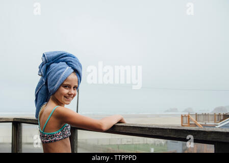 Portrait of happy girl with head wrapped in towel standing in balcony Stock Photo