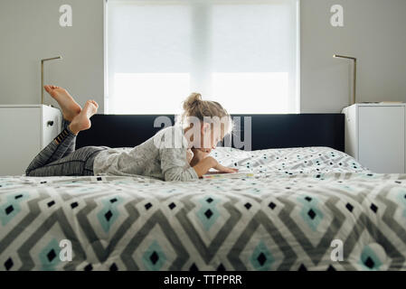 Side view of girl reading book while lying on bed at home Stock Photo