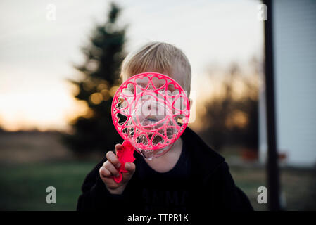 Boy blowing bubbles while standing at park during sunset Stock Photo