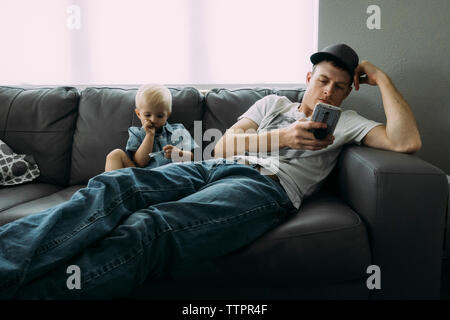 Father using phone while sitting by son on sofa at home Stock Photo