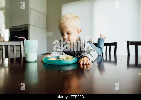 Baby boy eating food while lying on table at home Stock Photo