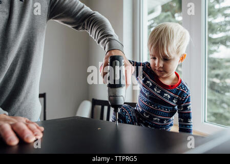 Midsection of father with son using drill on table at home Stock Photo