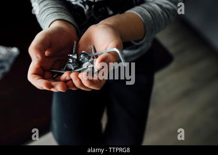 Midsection of boy holding drill bits while sitting on chair at home Stock Photo