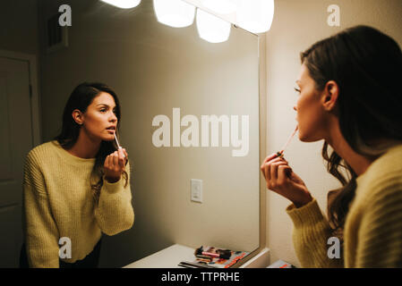 Woman applying lip gloss reflecting on mirror at home Stock Photo