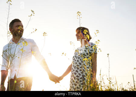 Man holding PRegnant woman's hand while standing on field against clear sky Stock Photo
